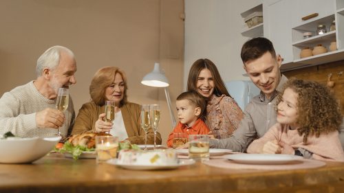 une famille de 6 personnes mange à table, les parents avec deux enfants et 2 grand-parents. Ils mangent tout en riant autour de la table.